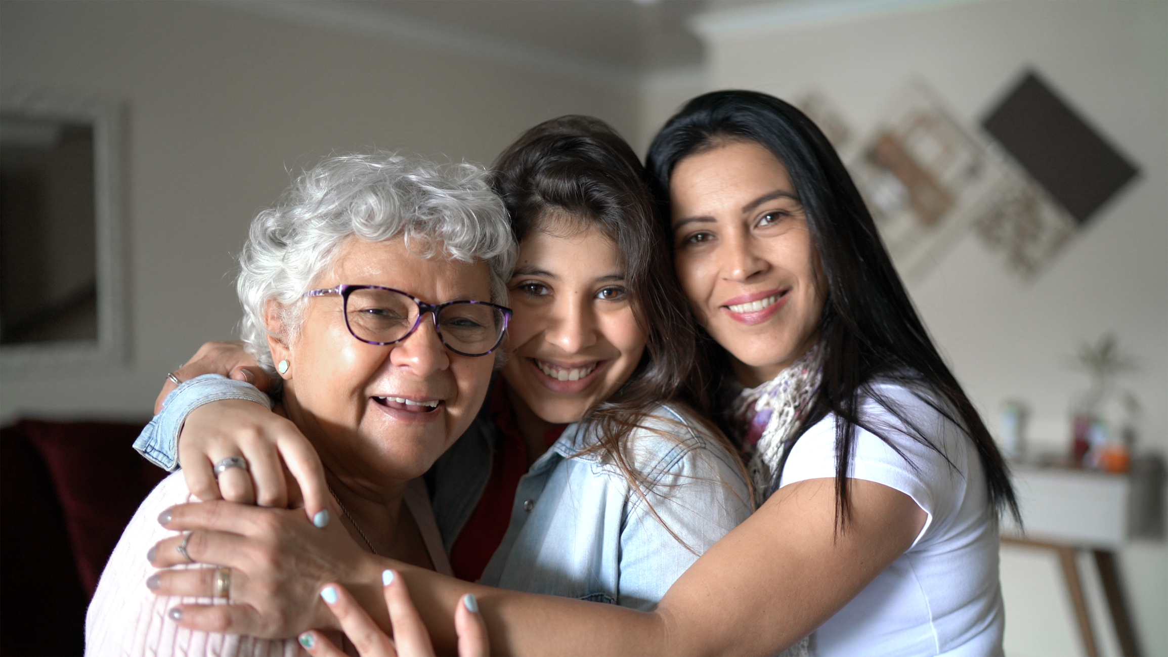 Three generations of women smile at the camera while hugging each other