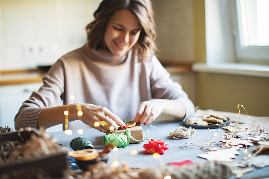 A woman smiles while wrapping a small holiday present at a table