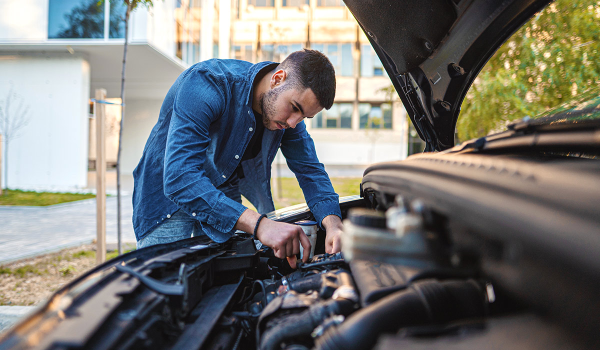 Man working under the hood of a car, conducting vehicle maintenance.